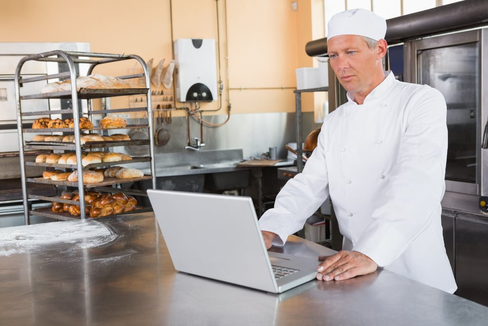 Focused baker using laptop on worktop in the kitchen of the bakery